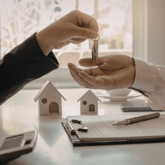 Manos intercambiando llaves, cerca de minicasas y un contrato inmobiliario.