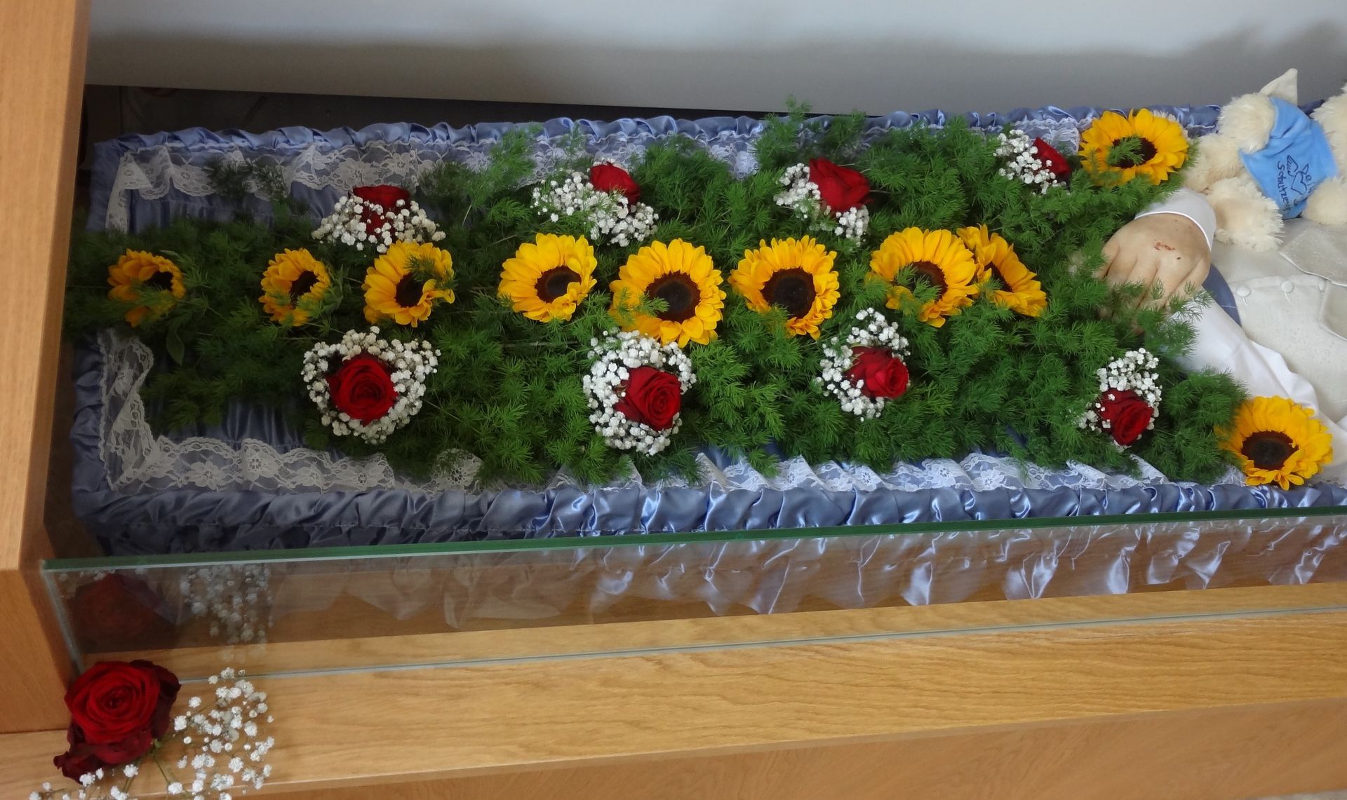 Ein Baby liegt in einem mit Sonnenblumen und Rosen geschmückten Sarg.