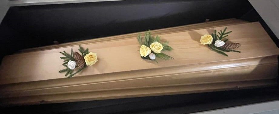 Ein Holzsarg mit drei Blumen darauf.