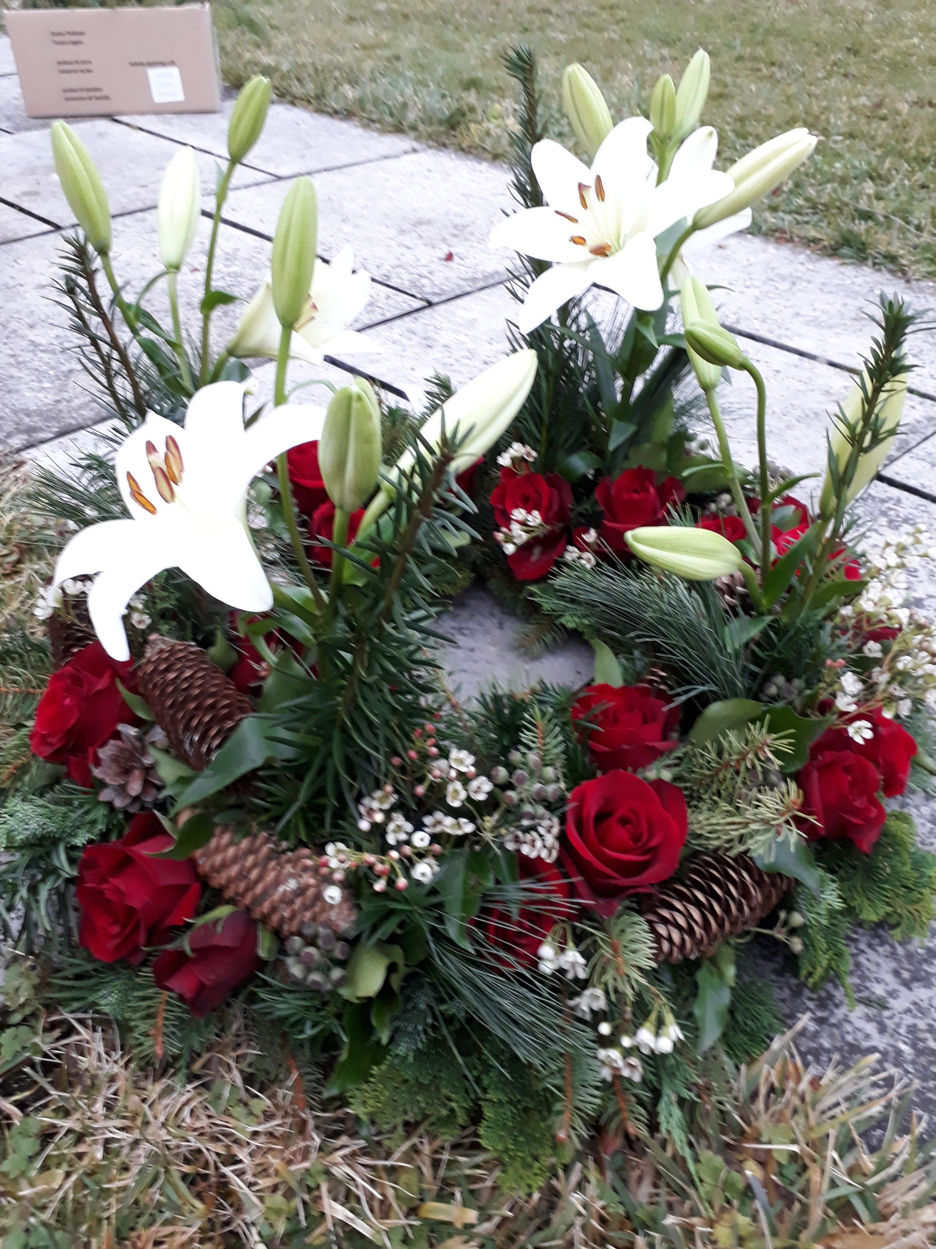 Auf einem Bürgersteig liegt ein Kranz mit roten Rosen und weißen Lilien.