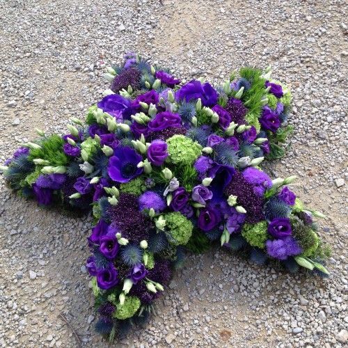 Auf dem Boden steht ein Kreuz aus violetten und grünen Blumen.