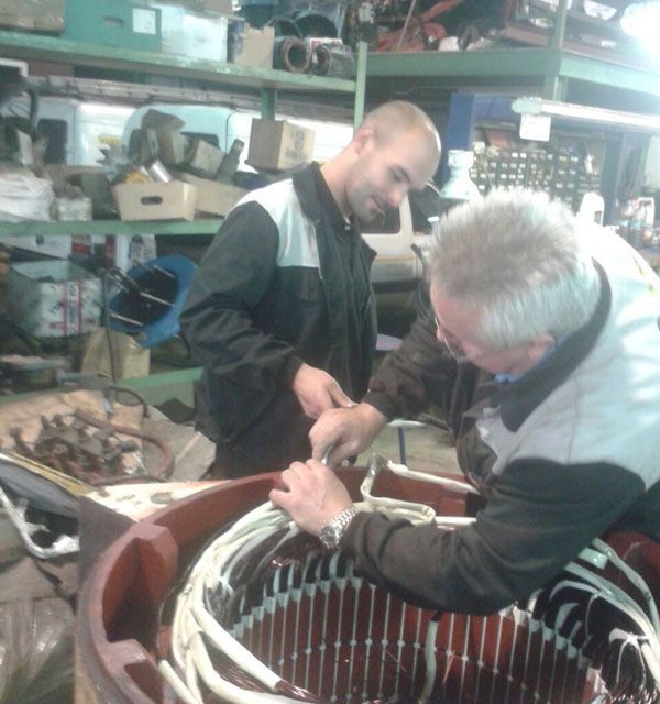 Dos hombres están trabajando en un motor eléctrico en un garaje.