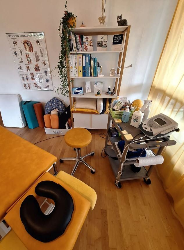 Ein Zimmer mit einem gelben Behandlungstisch und einem Hocker, Physiotherapie & Shiatsu Erika Rutten