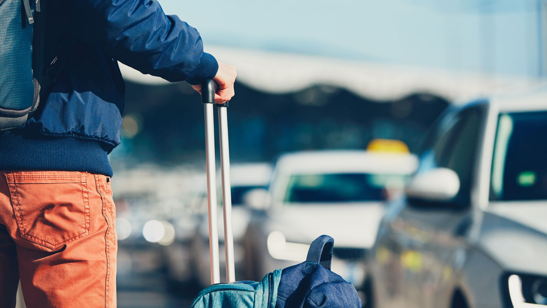 Une personne avec des bagages se tenant près de voitures, probablement dans un aéroport.