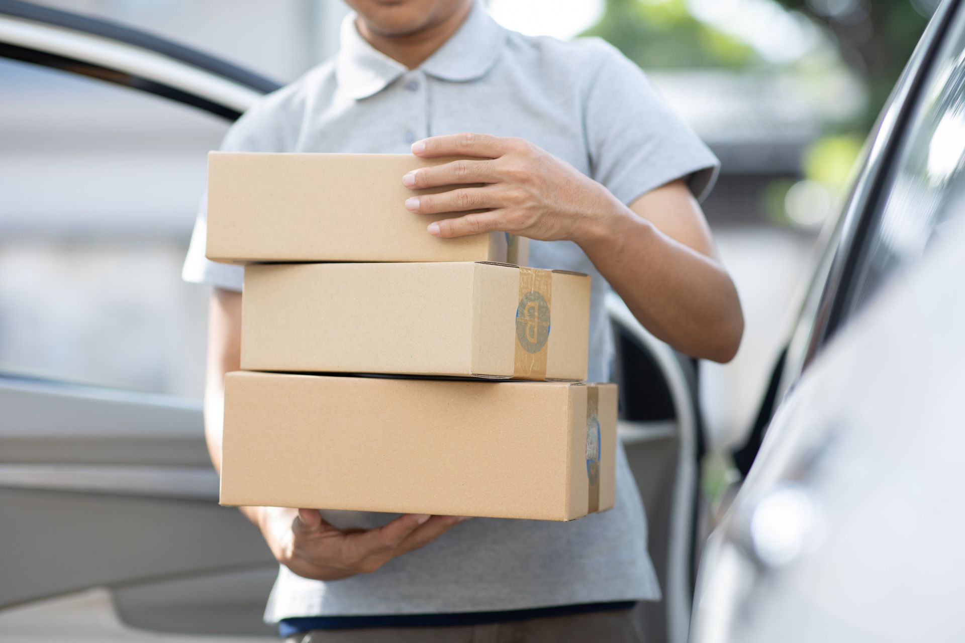 Une personne tenant trois cartons à côté d'une portière de voiture ouverte, se prépare à effectuer une livraison.