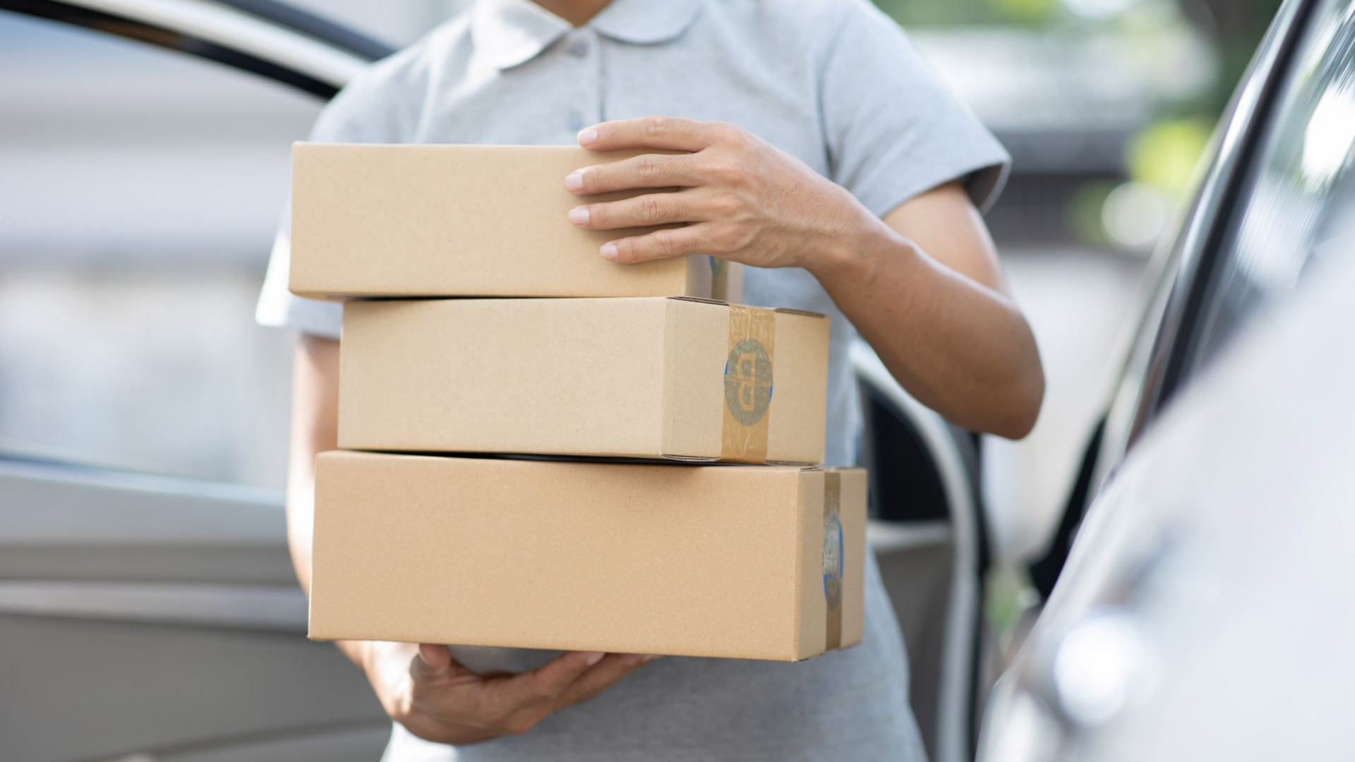 Une personne tenant une pile de trois cartons à côté d'une portière de voiture ouverte.