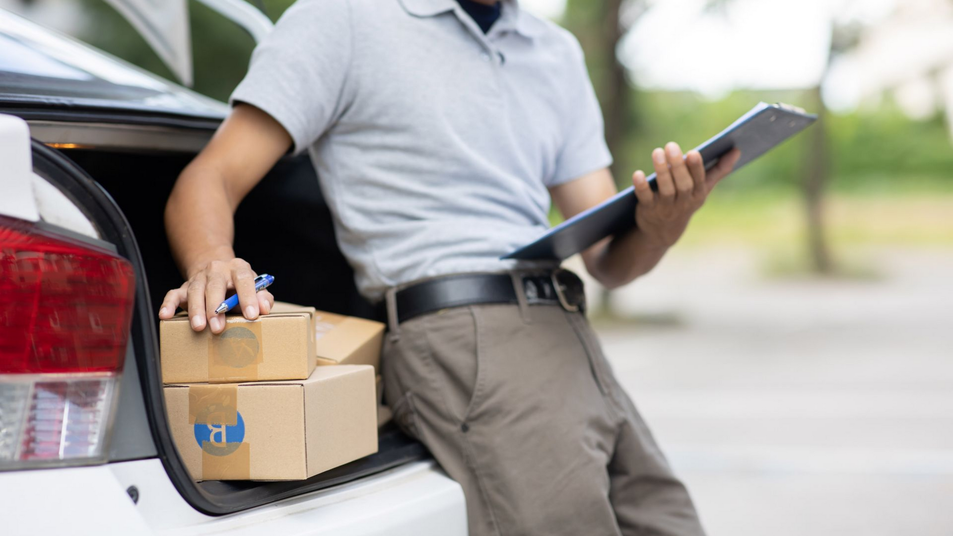 Livreur avec des cartons dans le coffre de sa voiture, tenant une tablette.
