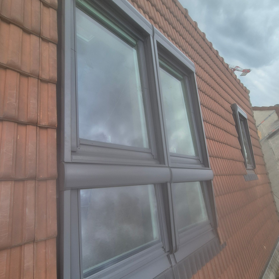 Puits de lumière ouvert sur un toit de tuiles rouges contre un ciel bleu clair.