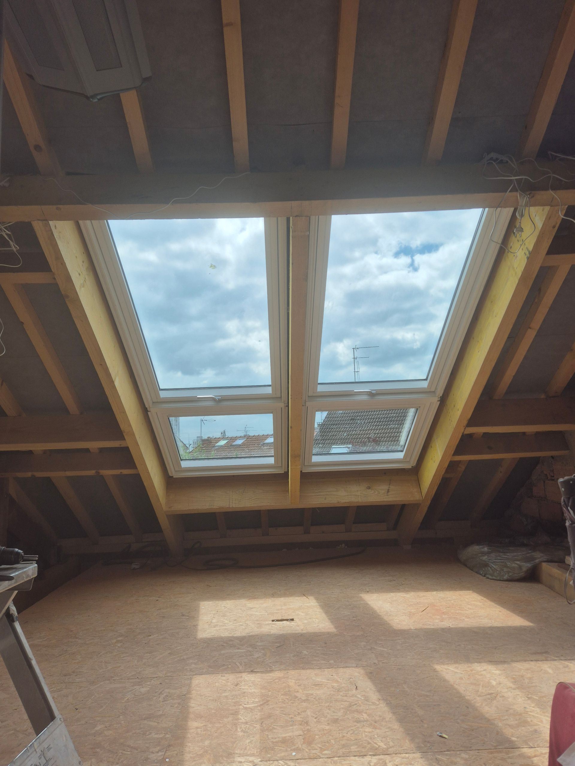Trois puits de lumière sur un toit en bardeaux foncés, reflétant une lumière chaude et dorée provenant des arbres environnants.