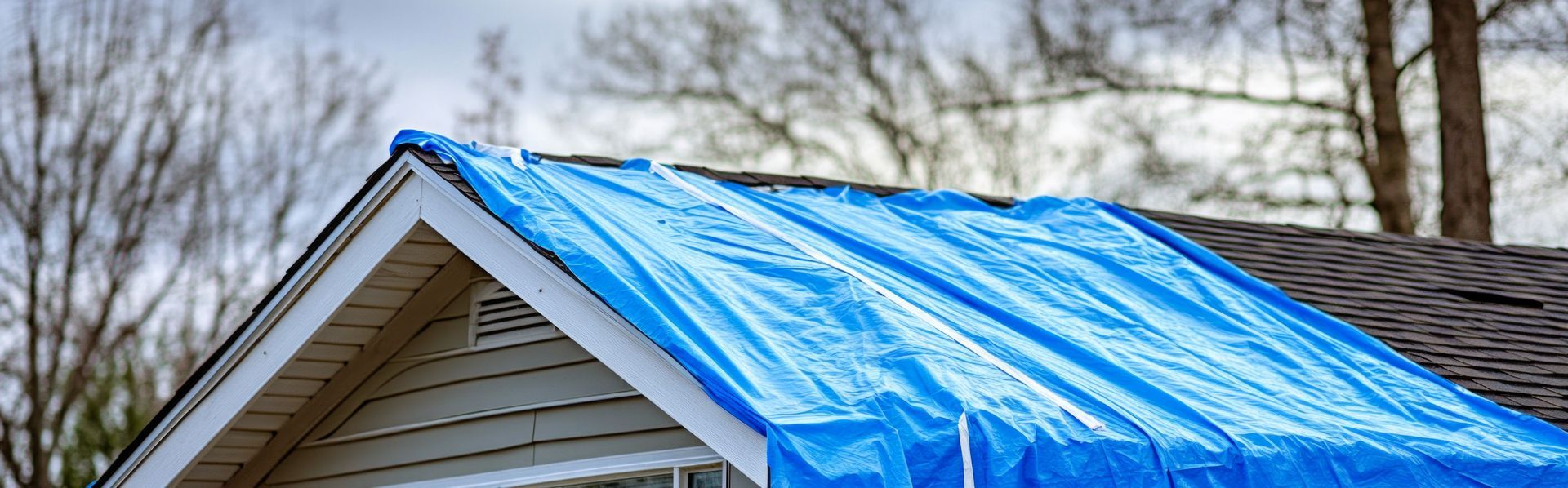 Une bâche bleue recouvre le toit endommagé d'une maison.
