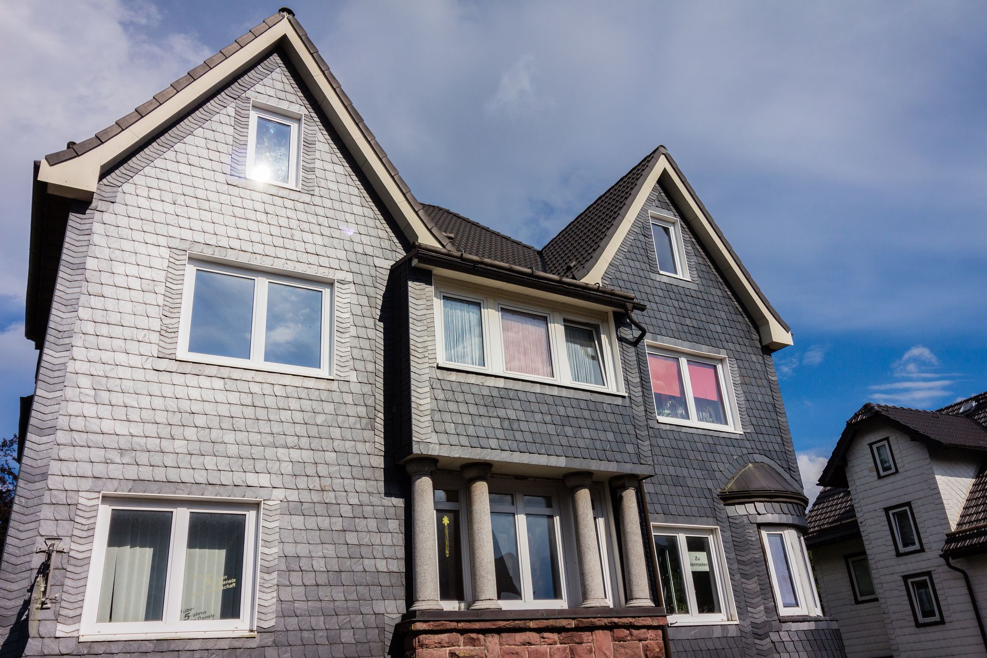 Maison en bardeaux gris avec plusieurs fenêtres sous un ciel bleu.