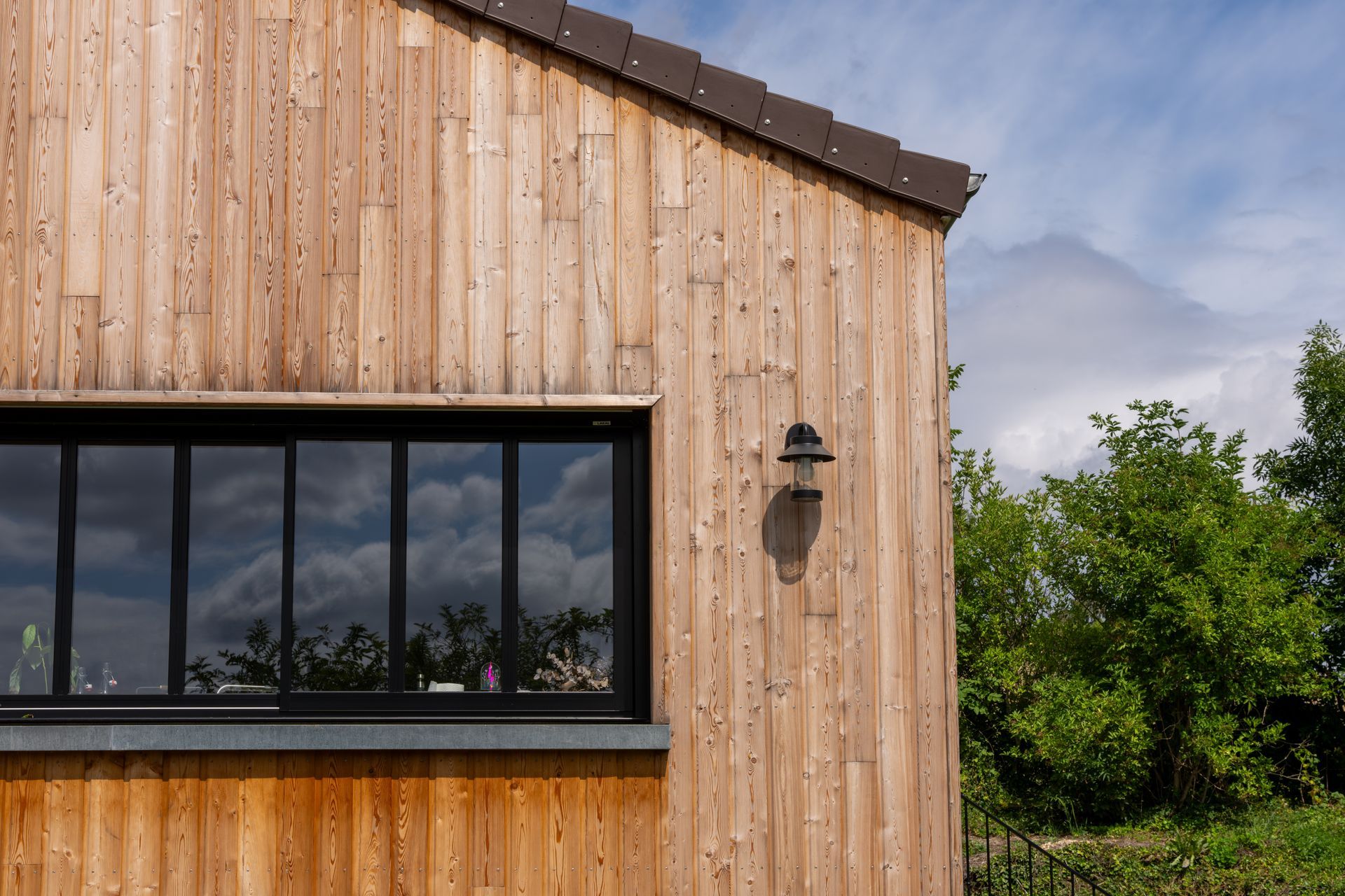 Extérieur d'un bâtiment en bois avec une fenêtre à cadre noir, un toit brun et un luminaire.