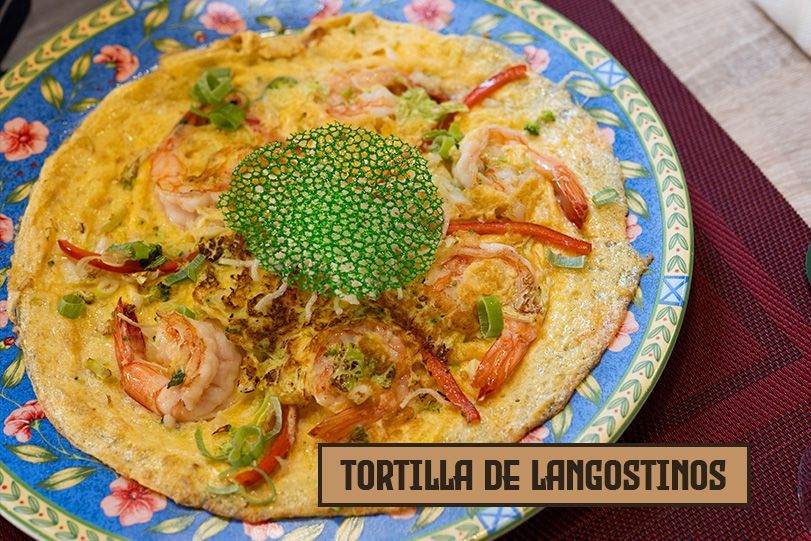 Tortilla de langostinos en un plato floral azul. La tortilla lleva camarones, pimientos y verduras.