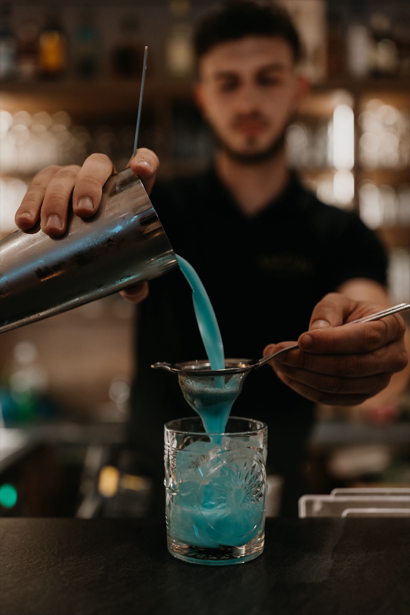 Ein Barkeeper gießt einen blauen Cocktail aus dem Shaker in ein Glas mit Eis.