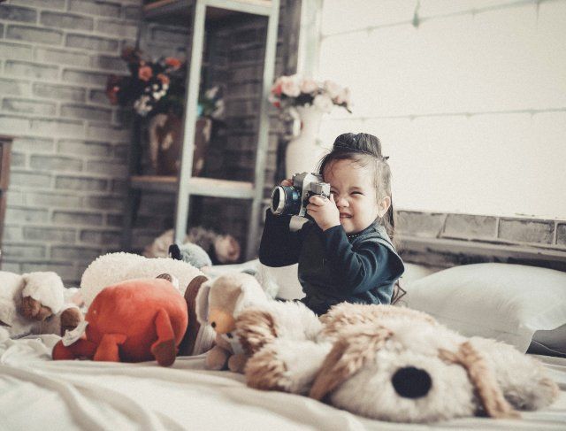 Activités Un enfant joue avec un appareil photo au milieu de peluches sur un lit.