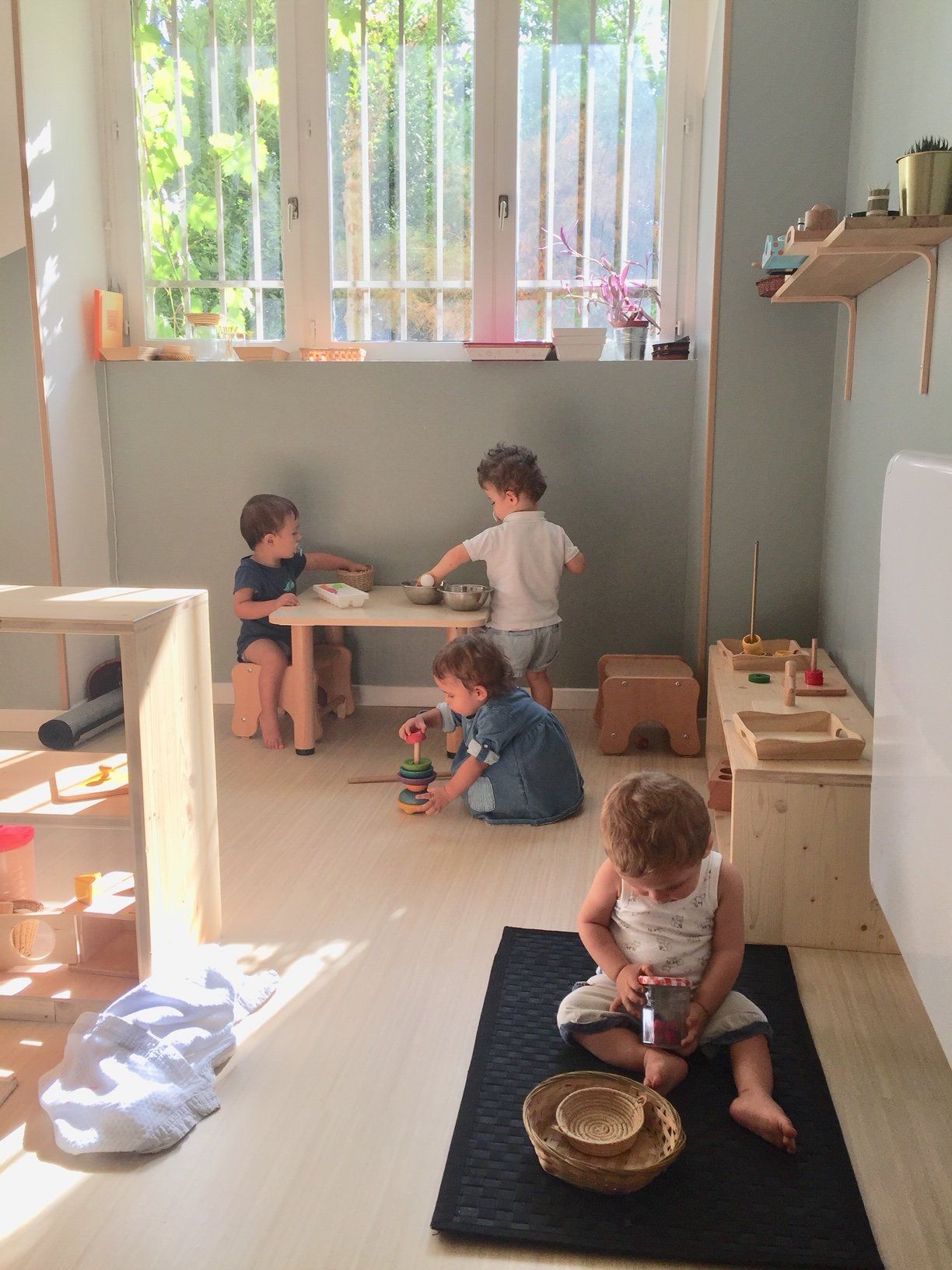 Des enfants jouent dans une crèche avec des jouets et une grande fenêtre
