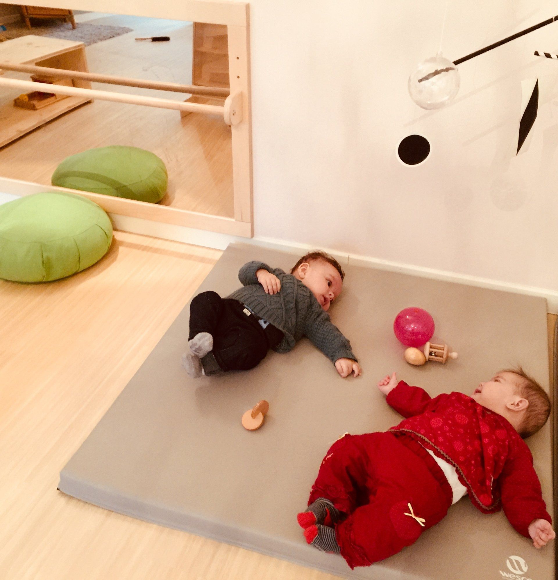 Deux bébés allongés sur des tapis de sol avec des jouets autour.