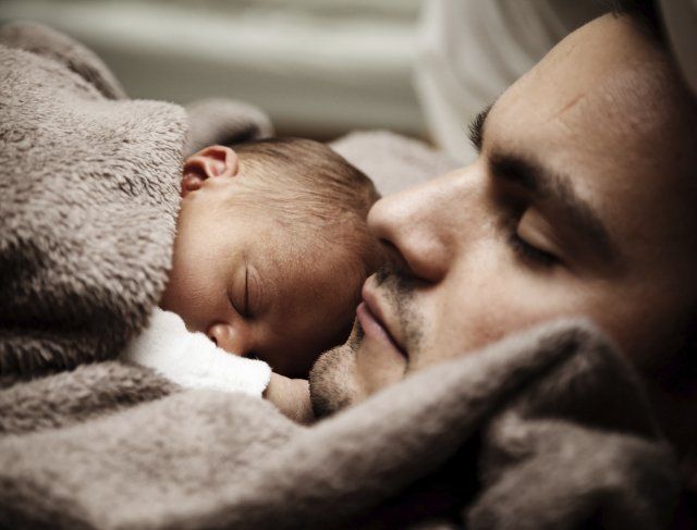 Relations Bébé endormi blotti contre un adulte sous une couverture beige