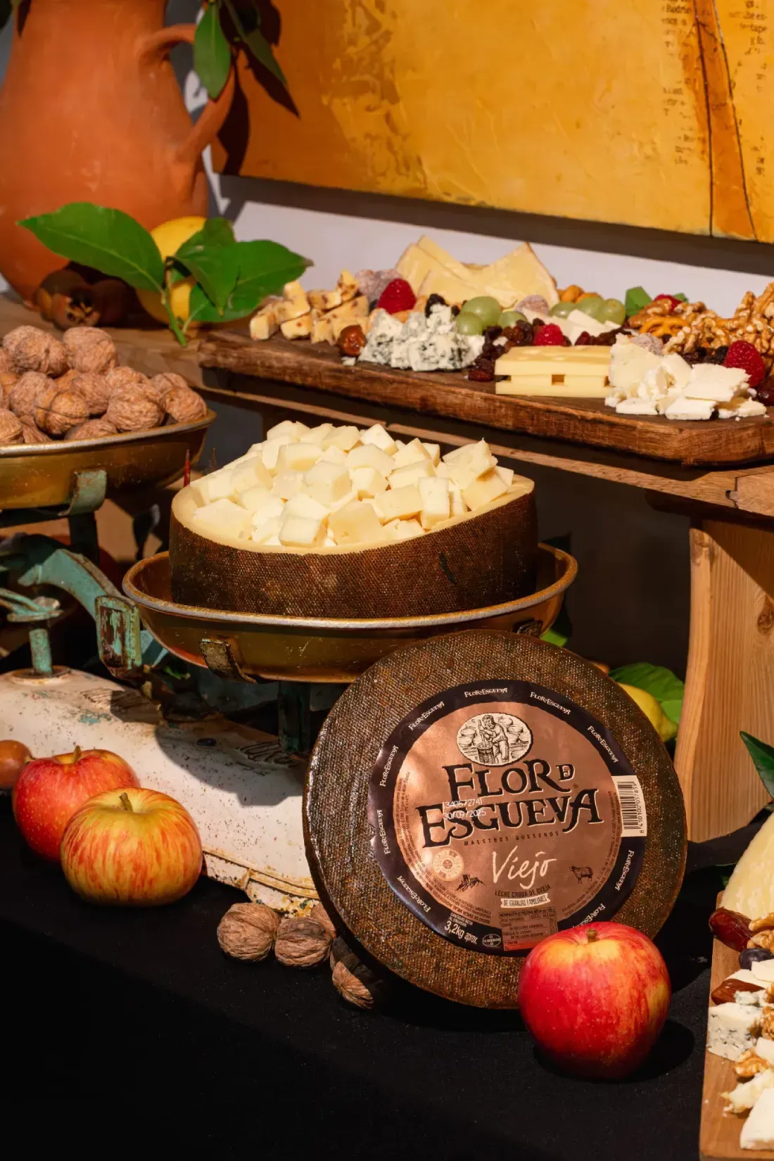 Exhibición de selección de quesos con manzanas, nueces y balanza.