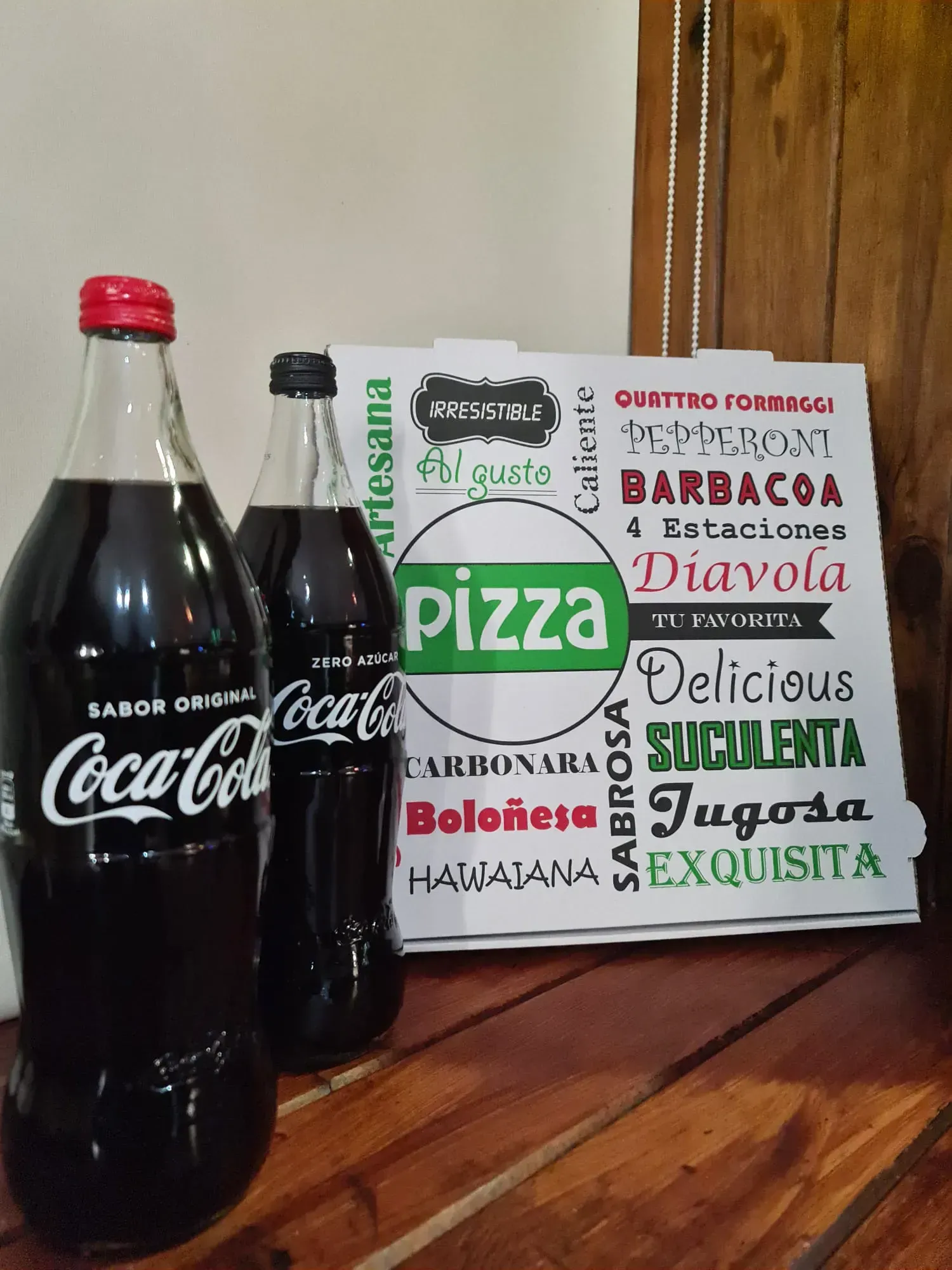 Dos botellas de Coca-Cola y una caja de pizza sobre una superficie de madera.