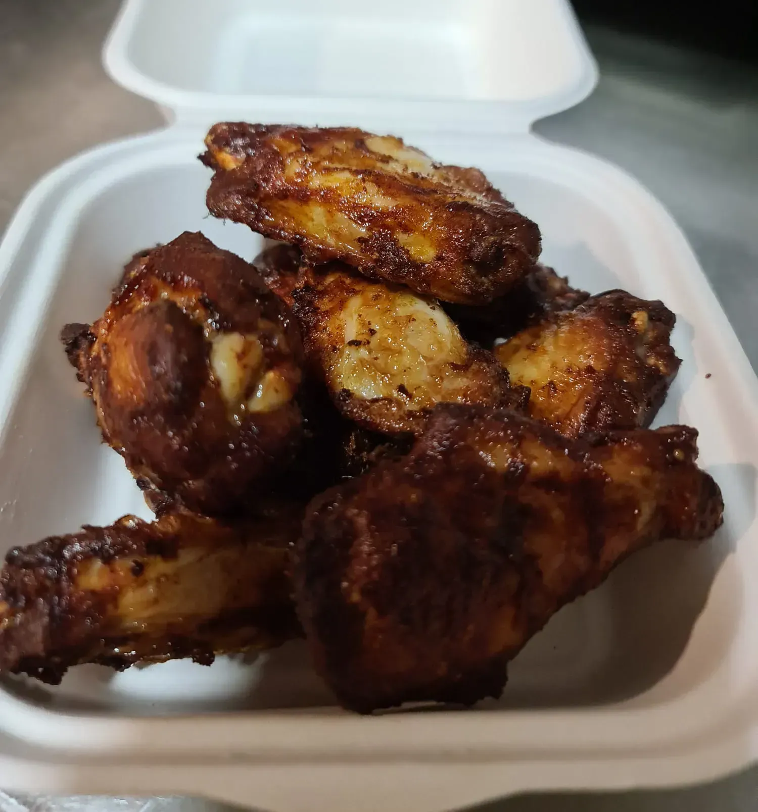 Pila de alitas de pollo cocidas en un recipiente blanco para llevar, doradas y brillantes.