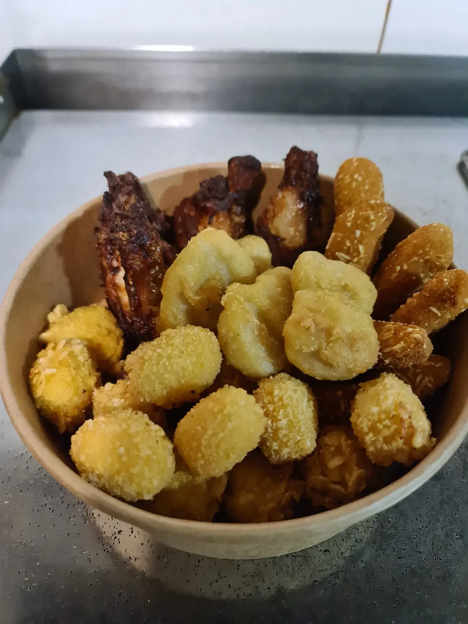 Tazón de alitas de pollo fritas, nuggets y otros alimentos rebozados.