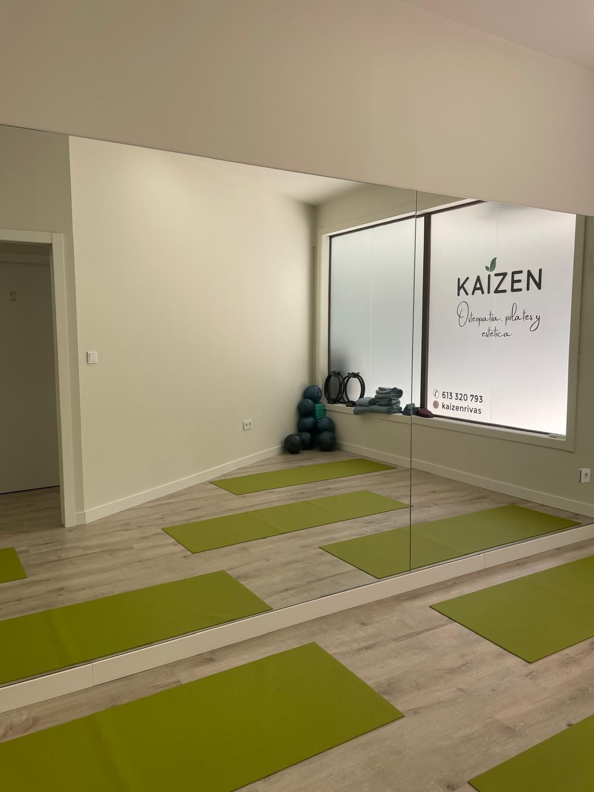 Una habitación con colchonetas de yoga verdes y un espejo grande.