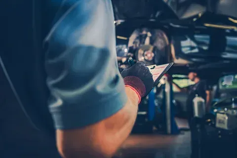 Un hombre sostiene una tableta en su mano mientras trabaja en un automóvil.