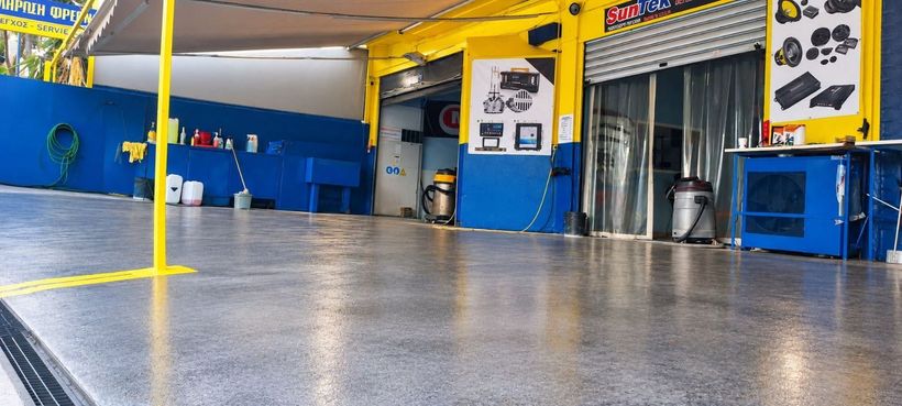 Άδειο εσωτερικό συνεργείου αυτοκινήτων με μπλε τοίχους, κίτρινες κολόνες και γυαλιστερό γκρι δάπεδο