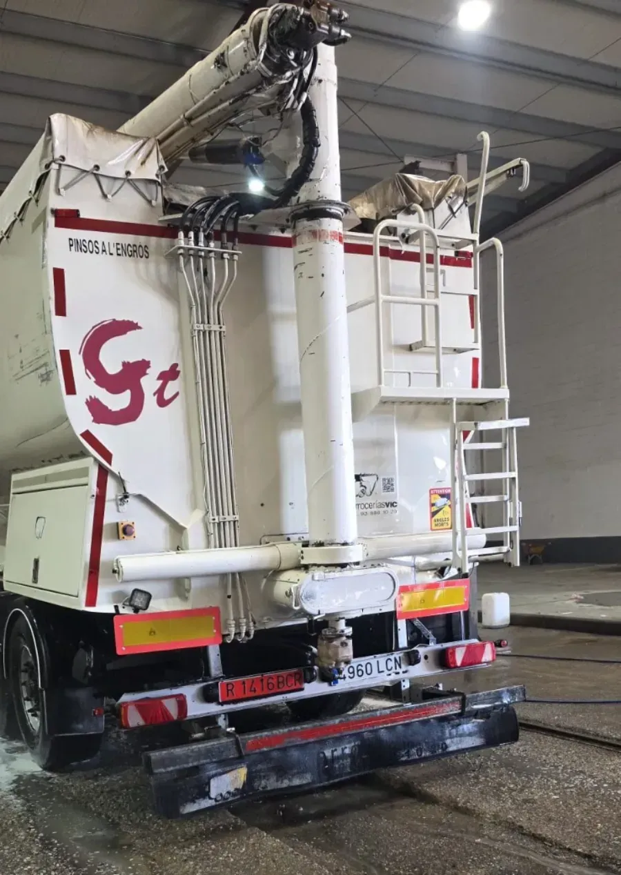 Camión aspirador industrial blanco con mangueras y escalera trasera estacionado dentro de un almacén.