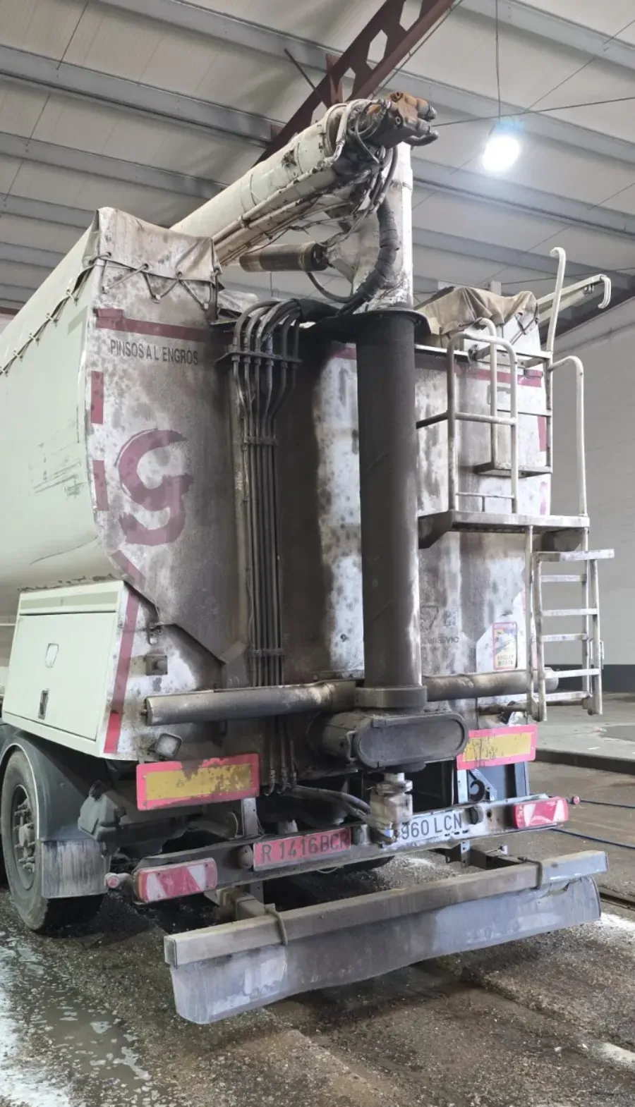 Parte trasera de un camión hormigonera sucio dentro de un almacén, con la tolva y el conducto de residuos