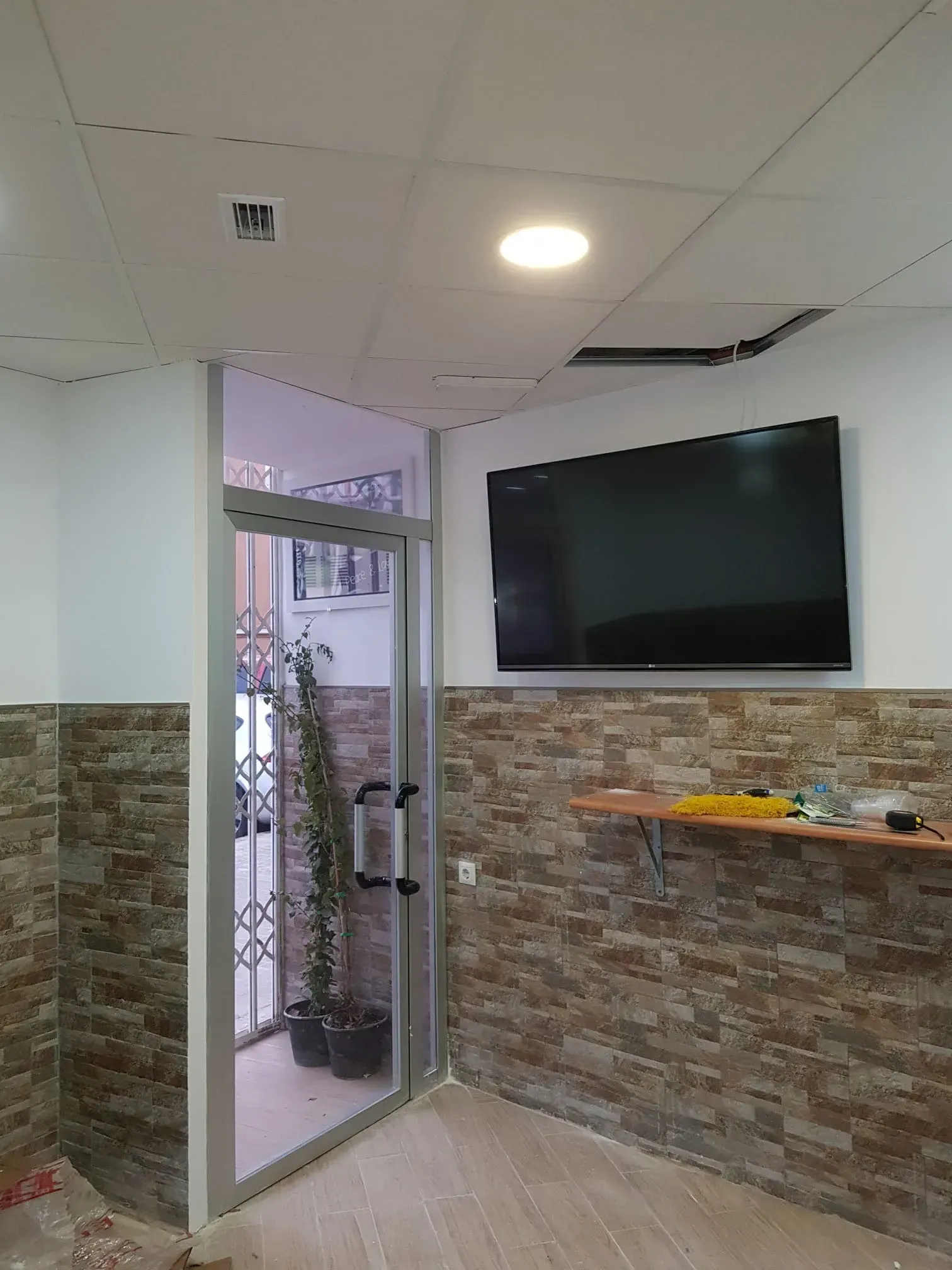 Vestíbulo moderno con televisor montado en la pared, puerta de cristal, pared decorativa de piedra y luces en el techo.