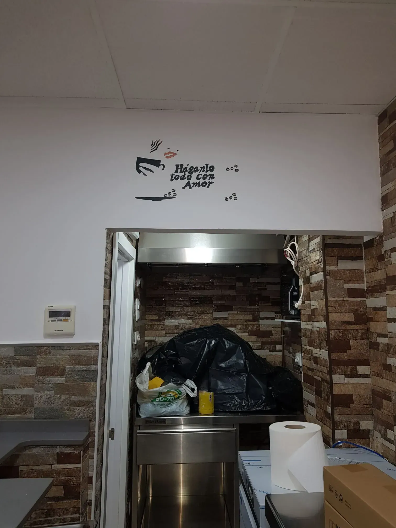 Pequeña ventana de servicio en la cocina con una bolsa de basura negra, encimera de acero inoxidable y paredes alicatadas en color marrón.