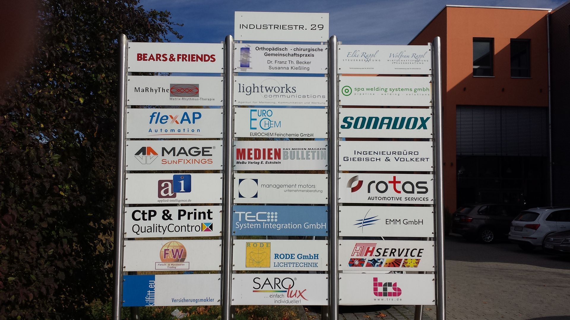 Schild mit mehreren Firmenlogos, das außerhalb eines Gebäudes angebracht ist.