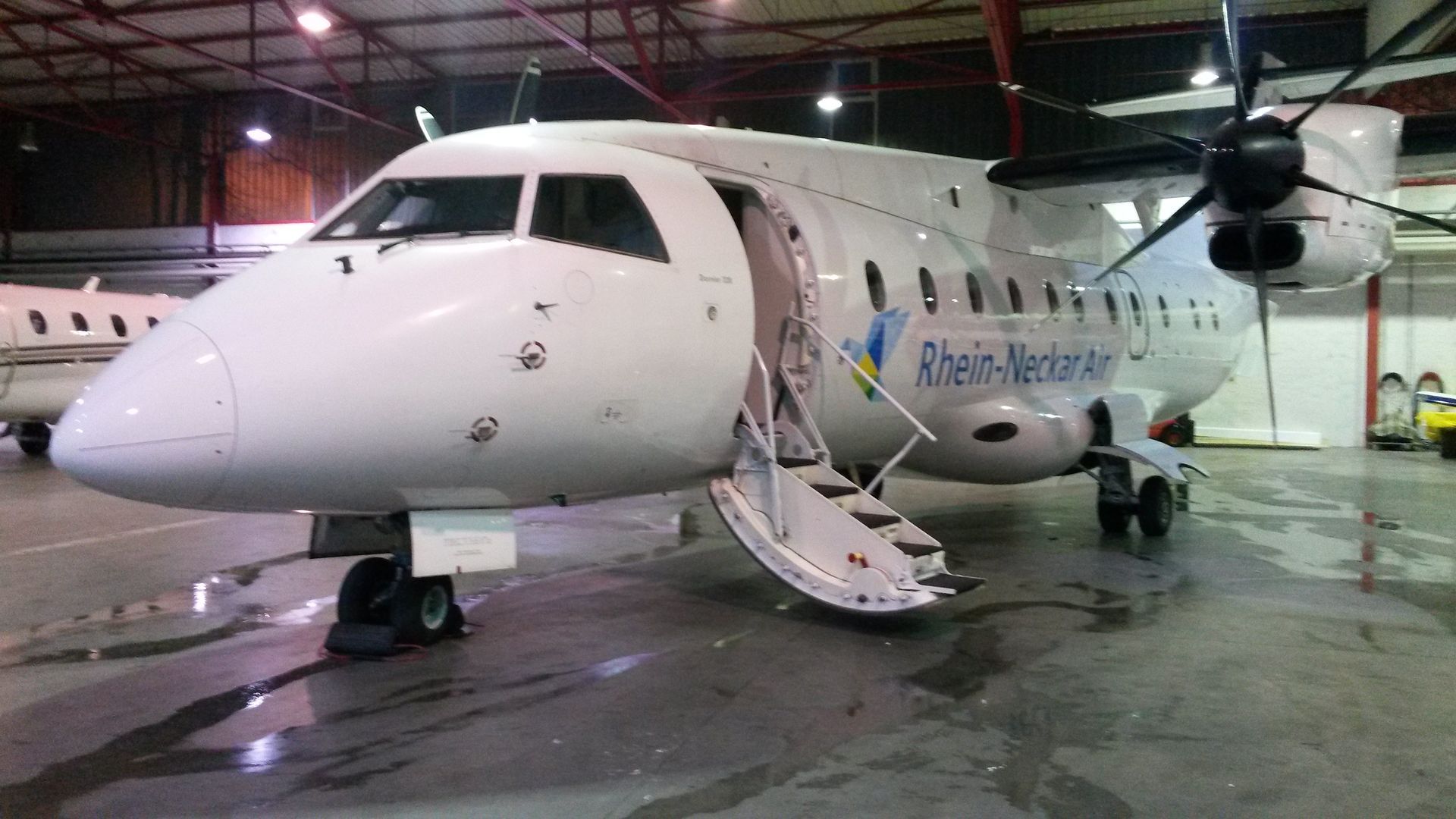 Weißes Turboprop-Flugzeug mit offener Tür in einem Hangar. „Ribeiro – Mendes“ an der Seite.