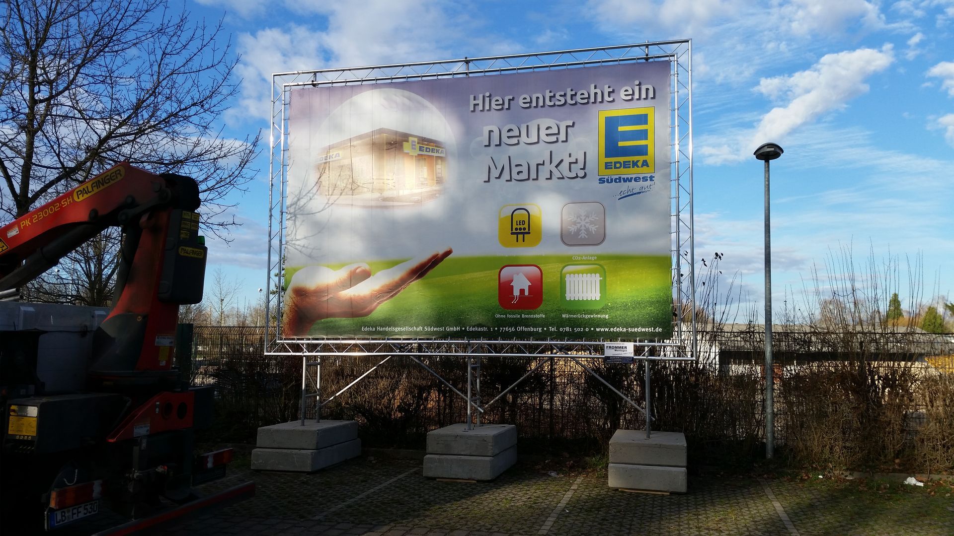 Plakatwand für den neuen Edeka-Markt, getragen von Metallrahmen und Betonblöcken.