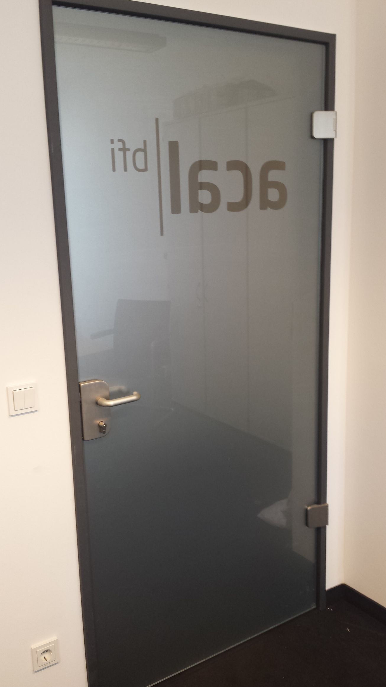 Glastür mit mattiertem Schriftzug „itd | 606“. Grauer Rahmen, Griff und Scharniere verchromt. Innenseite verdeckt.