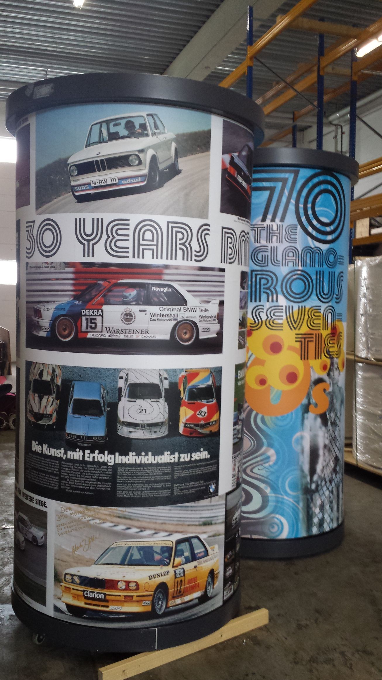 Zwei zylindrische Displays mit Rennwagengrafiken und Text, eines davon feiert „70 Jahre“.