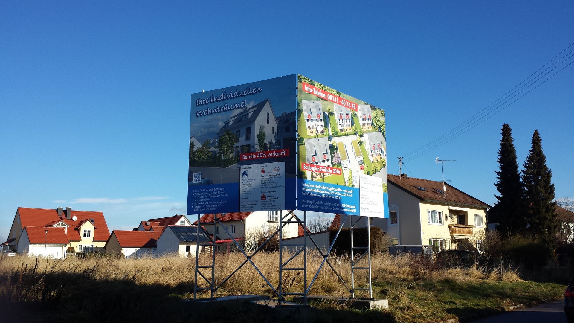 Große Werbetafeln mit Häusern vor blauem Himmel und Wohngebäuden.
