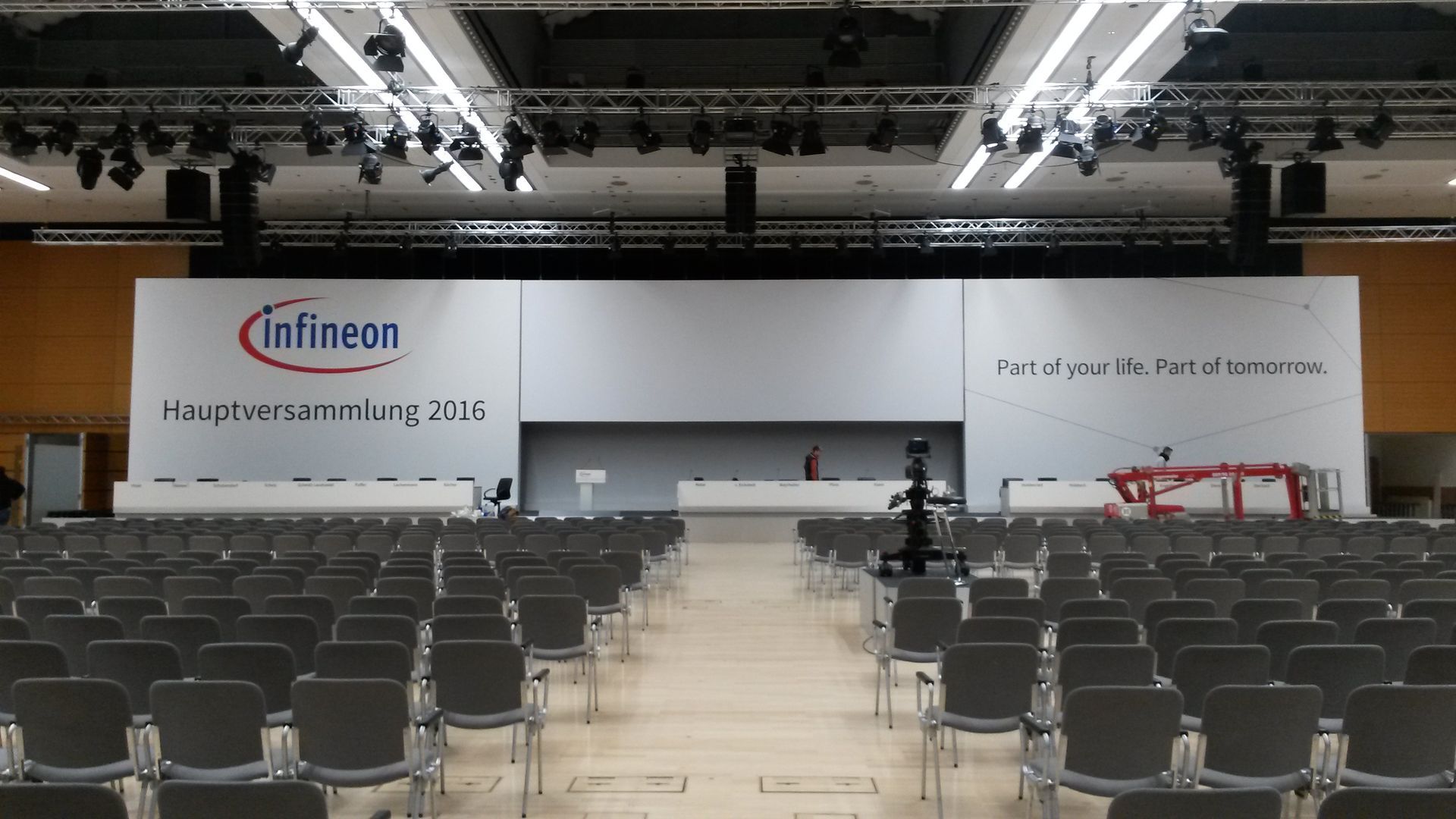 Leerer Zuschauerraum mit Stuhlreihen vor einer Bühne mit dem Infineon-Logo und dem Text „Hauptversammlung 2016“.