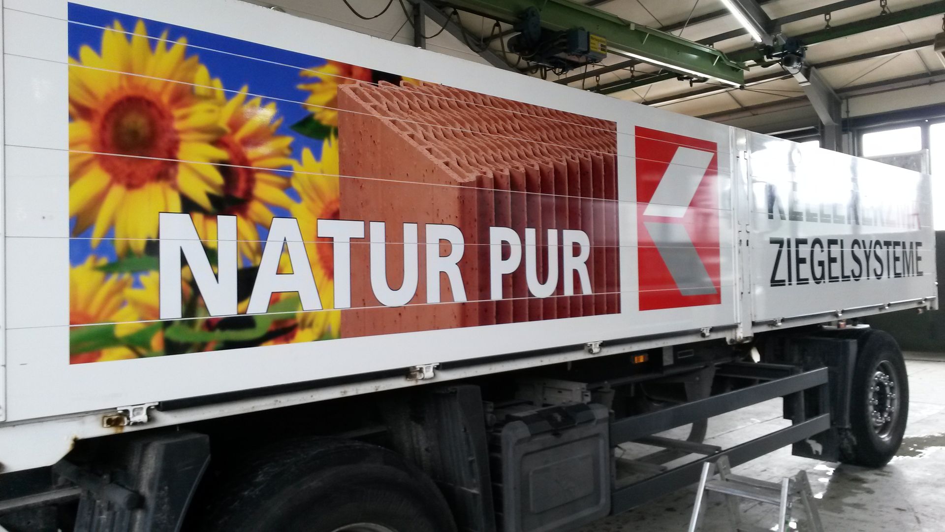 LKW mit den Aufschriften „NATUR PUR“ und „ZIEGELSYSTEME“, Sonnenblumen und Dachziegelgrafiken.
