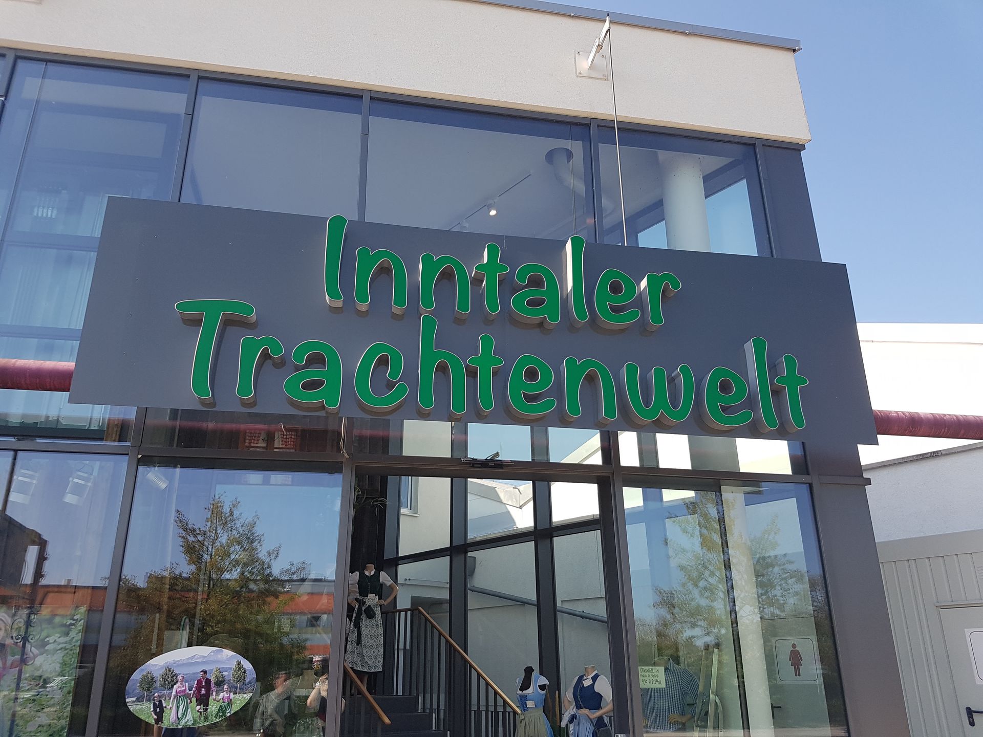 Leuchtbuchstaben „Inntaler Trachtenwelt“ über einem Glastüreingang.
