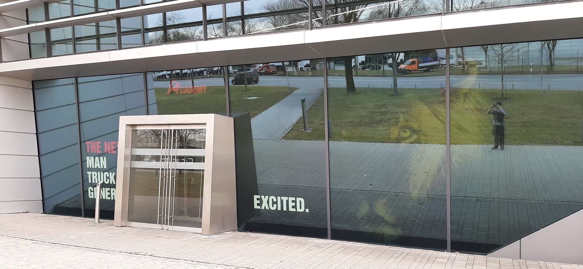 Ein modernes Gebäude mit reflektierendem Glas. Eine Person steht in der Spiegelung.