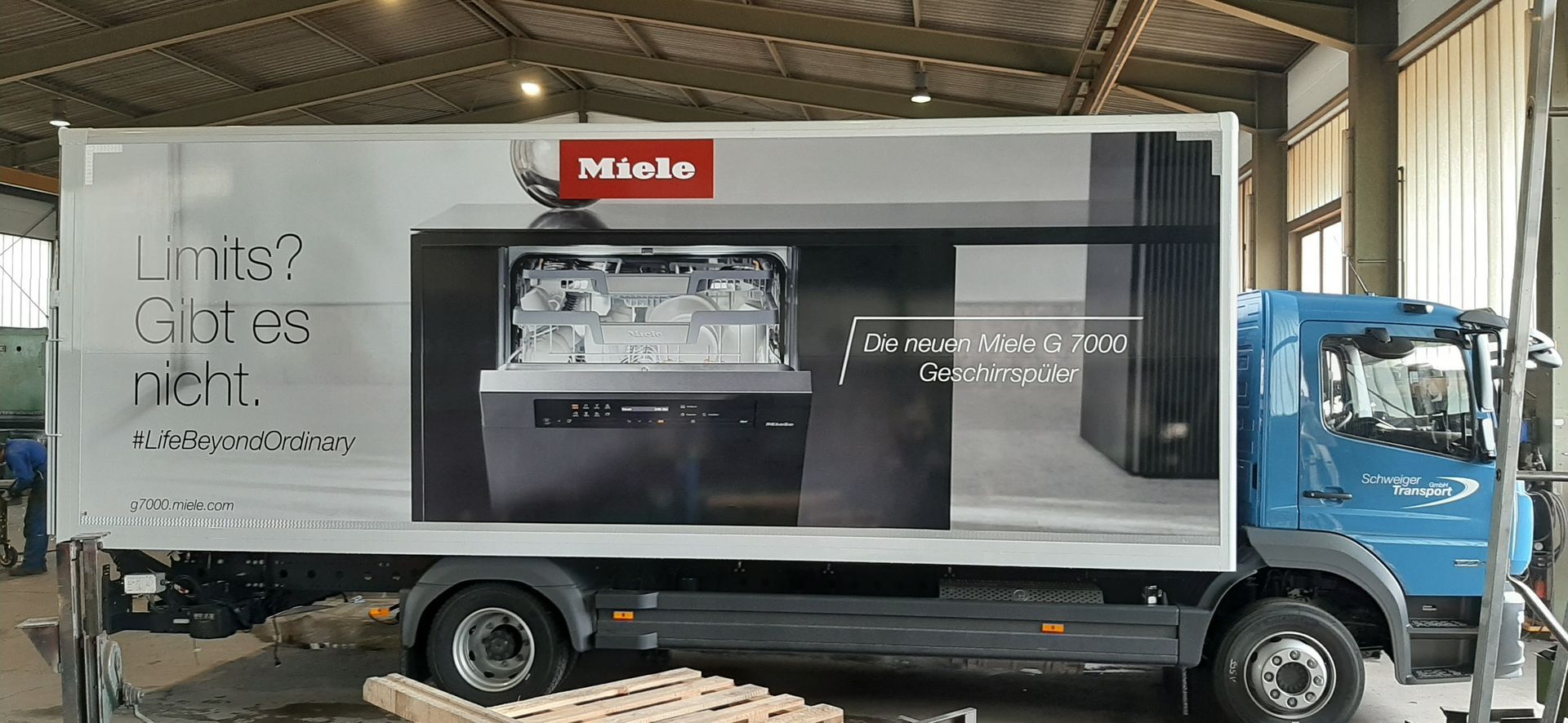 LKW mit Miele-Gerätewerbung. Blaues Fahrerhaus. Auf der Seitenwerbung ist ein Geschirrspüler abgebildet.