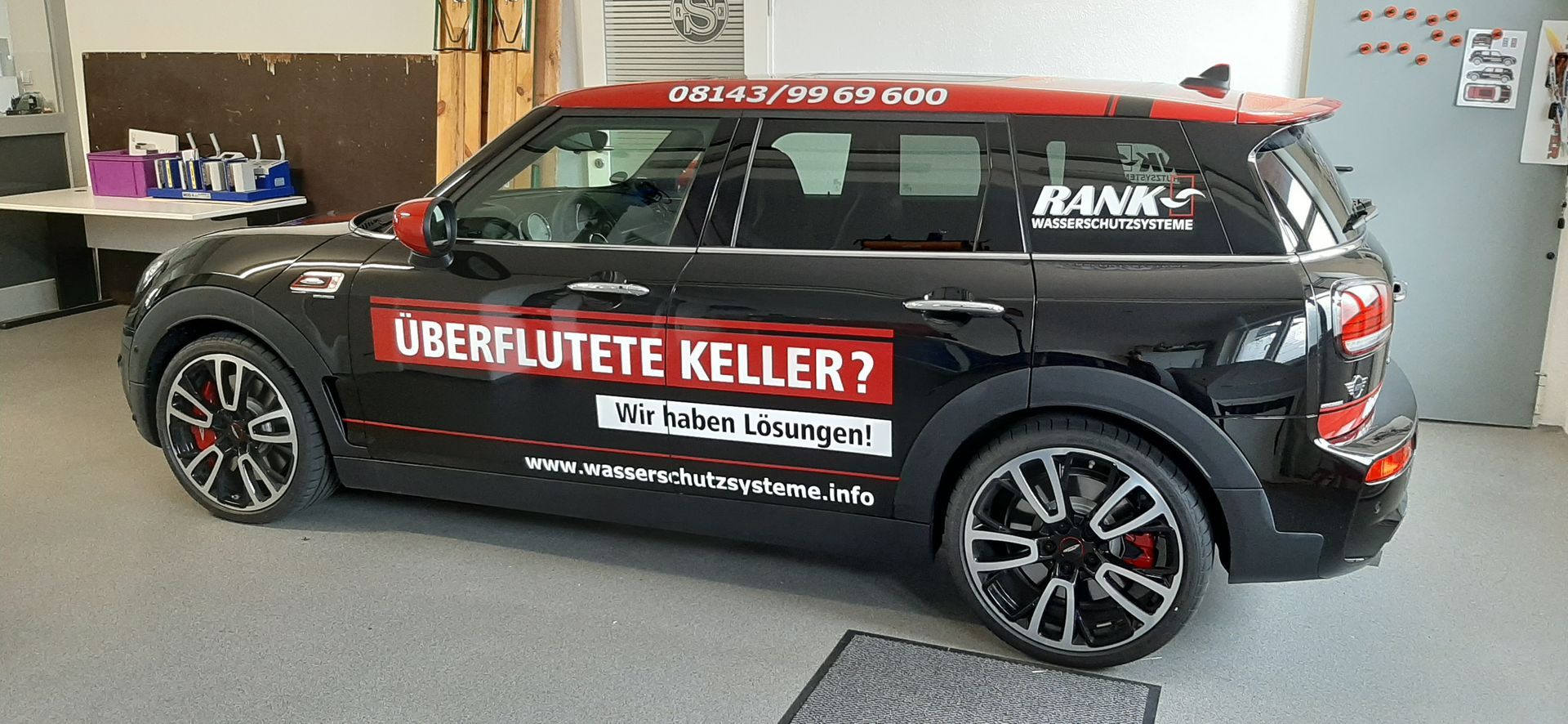 Schwarzer Mini Cooper mit roten Akzenten und Werbung für „Überflutete Keller?“