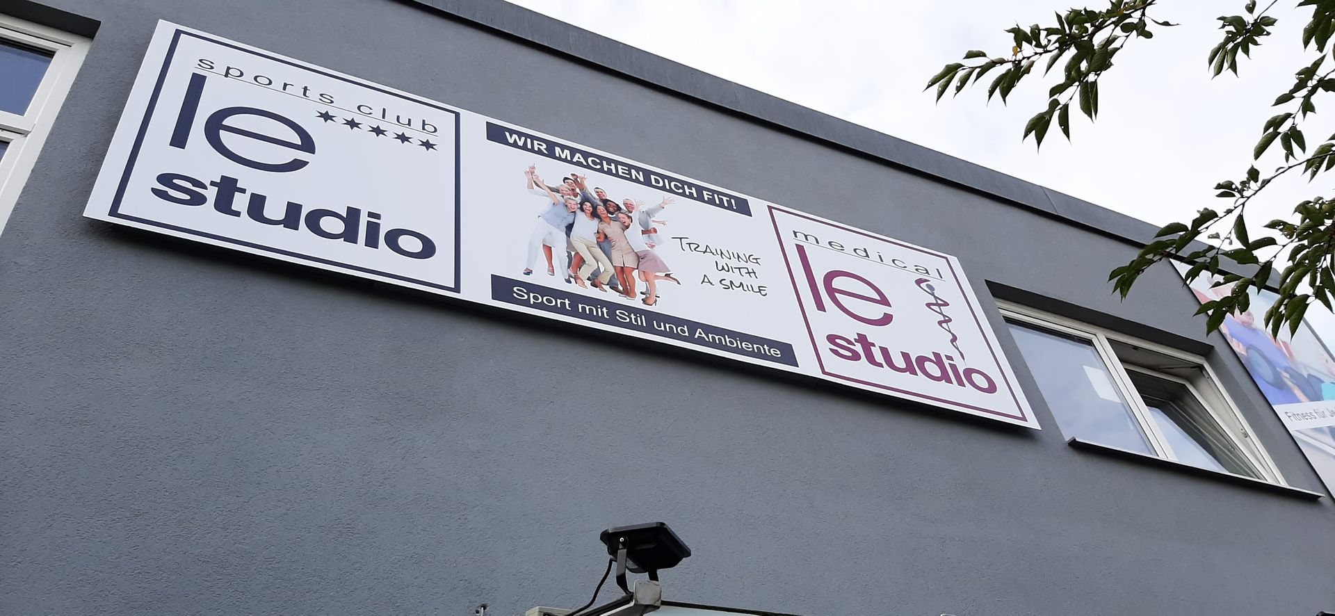 Schild für das Fitnesscenter „Le Studio“ an einem grauen Gebäude.