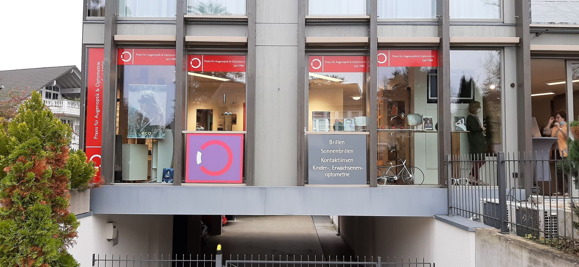 Ein Gebäude mit großen Fenstern. Vor einem Fenster steht ein lila Ständer mit einem kreisförmigen Logo.
