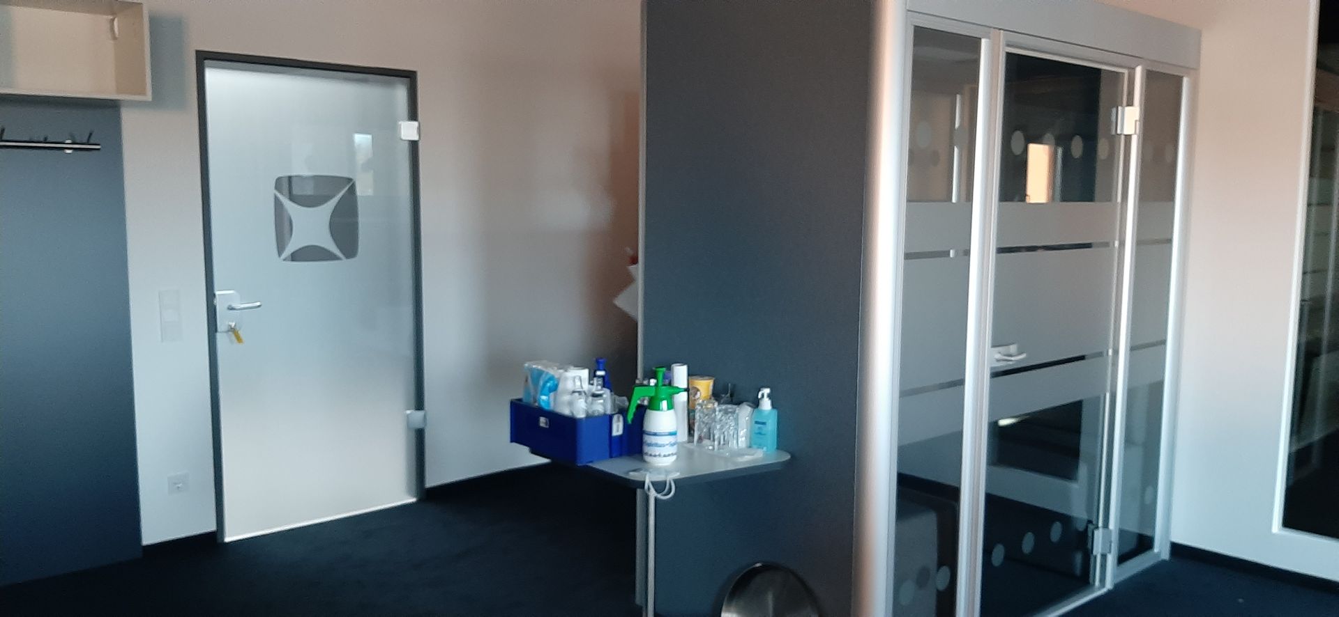 Büroinnenraum mit einer Milchglastür, einem Schreibtisch mit Vorräten und einem Raum mit Glaswänden.
