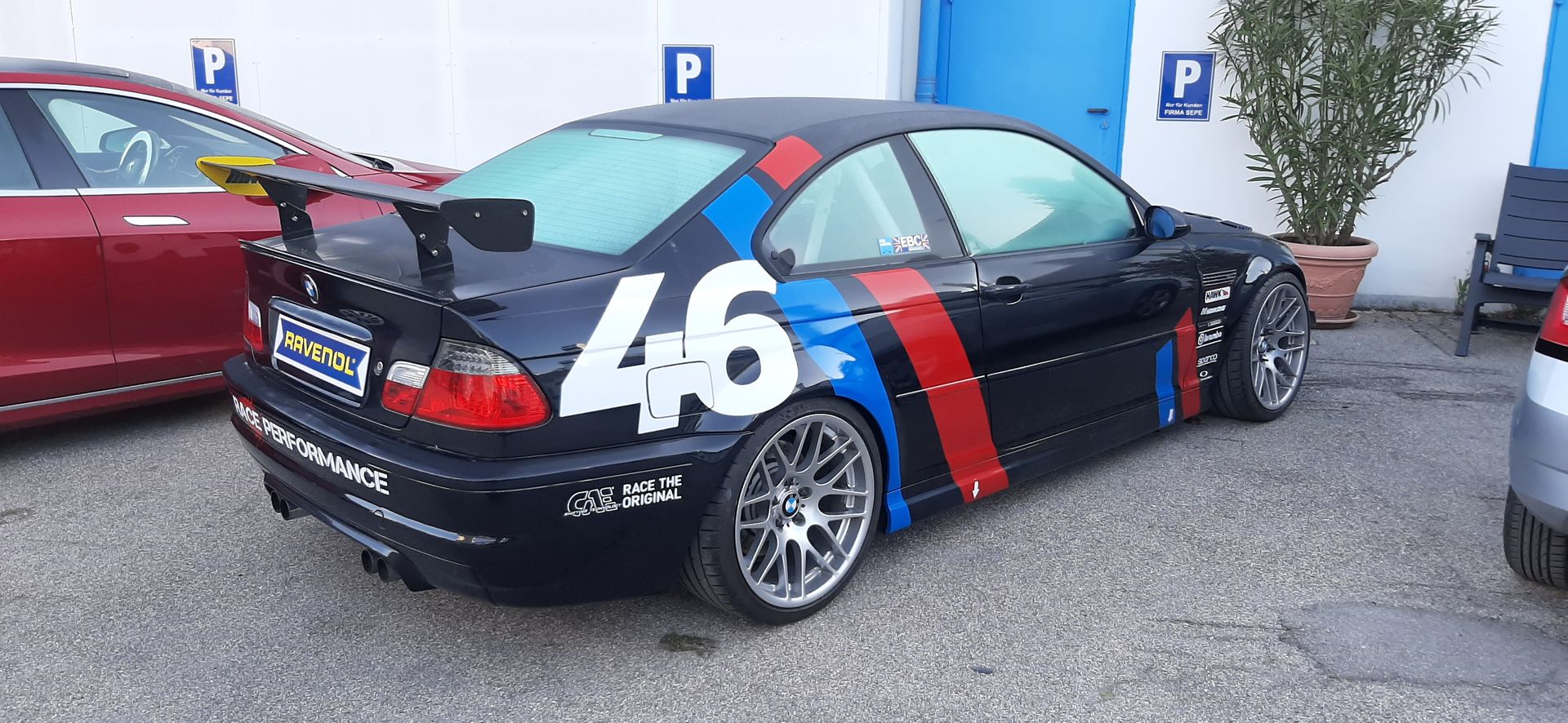 Schwarzer BMW-Rennwagen mit der Nummer 46 und roten, blauen und weißen Streifen. Draußen geparkt.