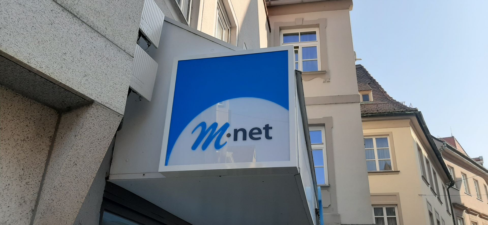 Ein blau-weißer „M.net“-Leuchtkasten an einem Gebäude.